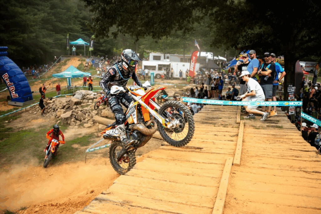 Sam competes in a challenging rock garden section of the Red Bull Tennessee Knockout, with a Red Bull arch and a crowd of spectators in the background.