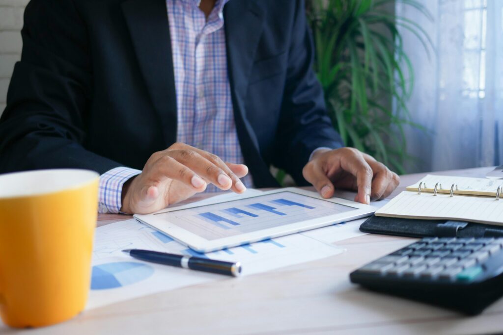 A business professional reviewing Google Ads performance data on a tablet, with printed charts and a calculator on the desk — analyzing where landscaping ad spend is going and identifying hidden budget leaks.
