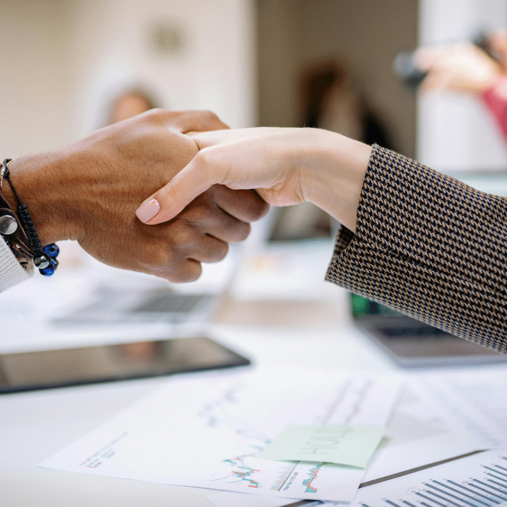 Two professionals shaking hands over marketing reports and analytics documents