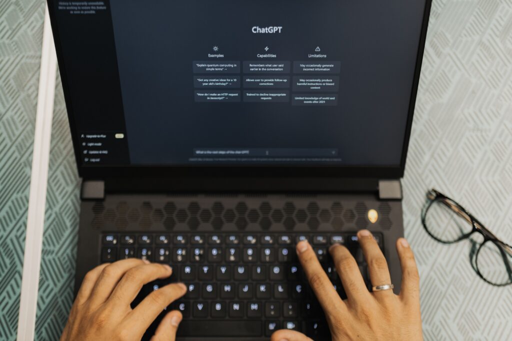 An overhead shot of a person's hands typing on a laptop keyboard with the ChatGPT interface open on the screen, optimizing content to rank in AI search results.