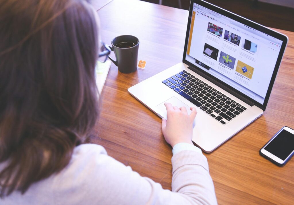 An over-the-shoulder view of a woman sitting at a wooden desk, analyzing a website layout on her laptop screen to improve its visibility in generative AI search results.