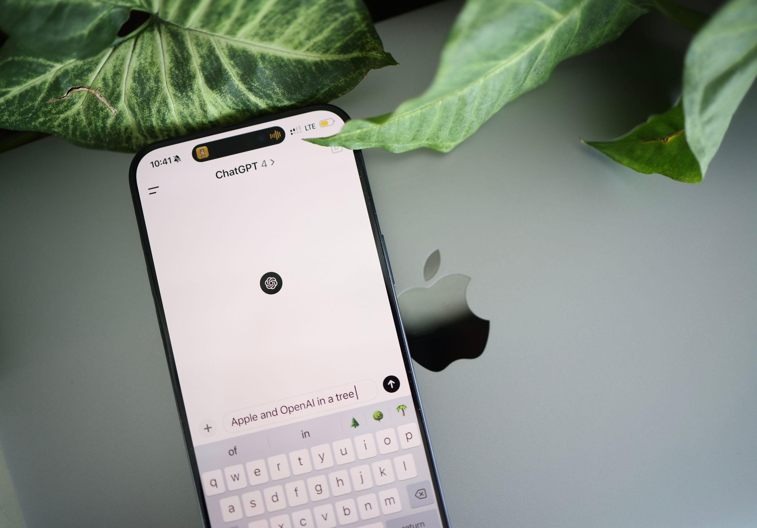 ChatGPT mobile app open on iPhone next to MacBook with green plants in background