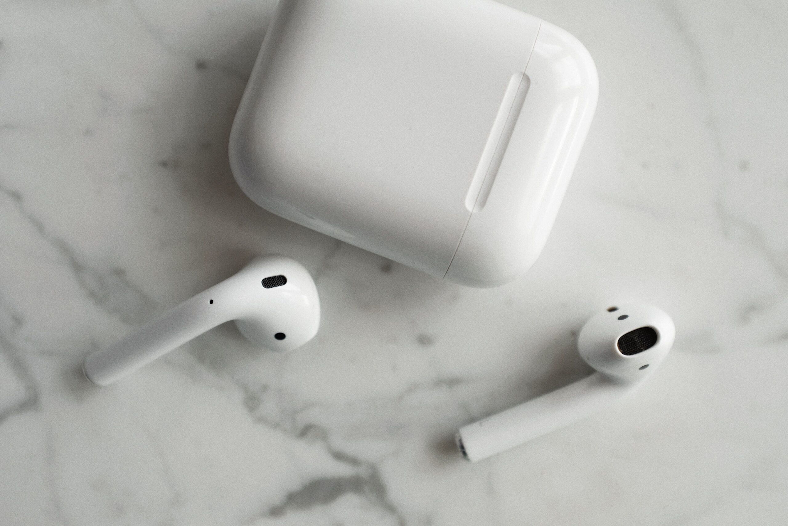White AirPods and charging case on a white marble surface
